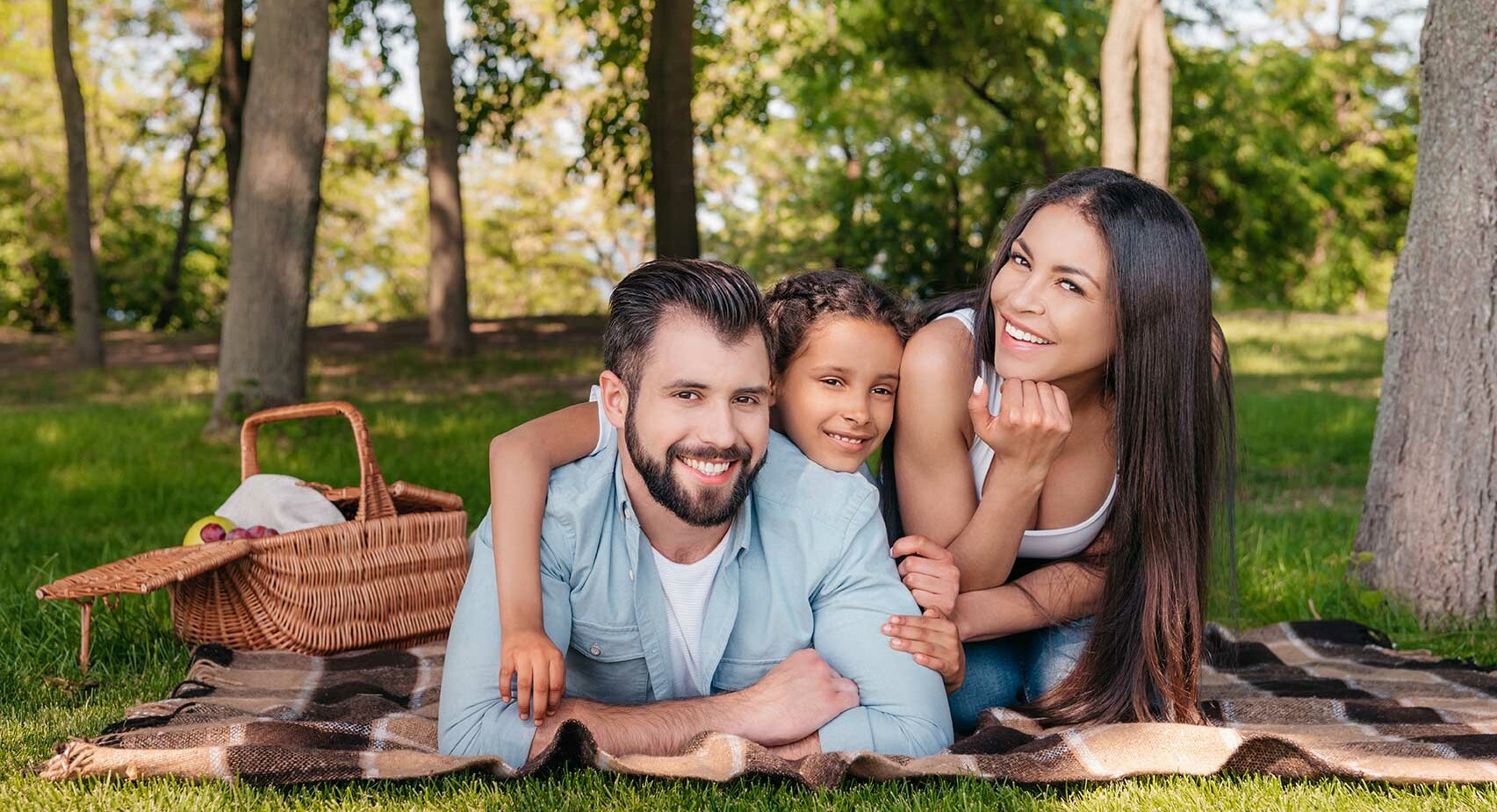A healthy, happy family of three, consisting of a father, mother, and a child, enjoying a picnic outdoors, smiling contentedly.