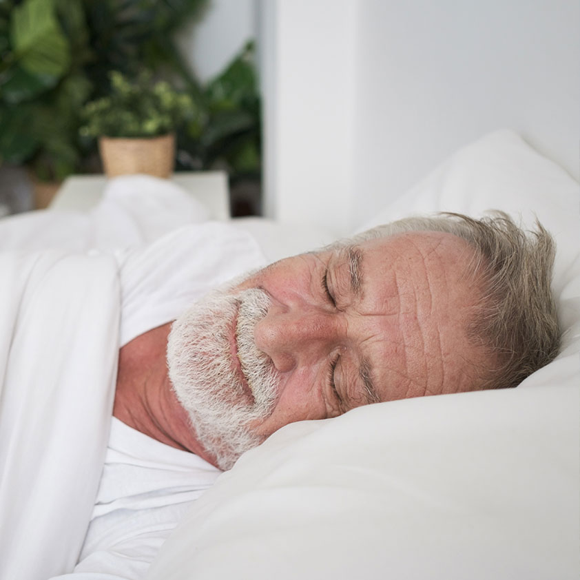 A man peacefully sleeping in bed, depicting a comfortable and restful sleep without suffering from sleep apnea.