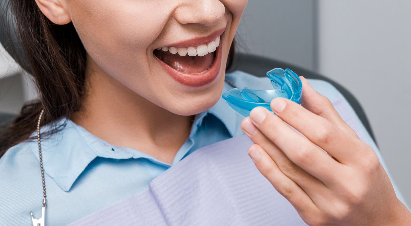 A woman holding a blue dental retainer, smiling showing her heathy straight teeth.