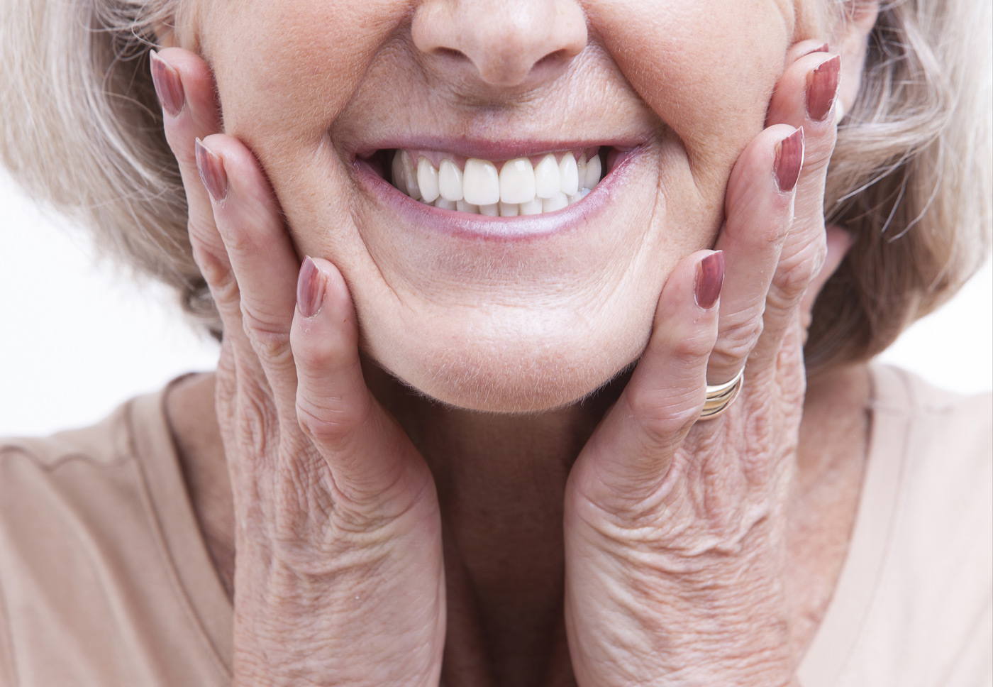 An elderly woman grimacing with clenched teeth, hands pressed against her cheeks, expressing bruxism.