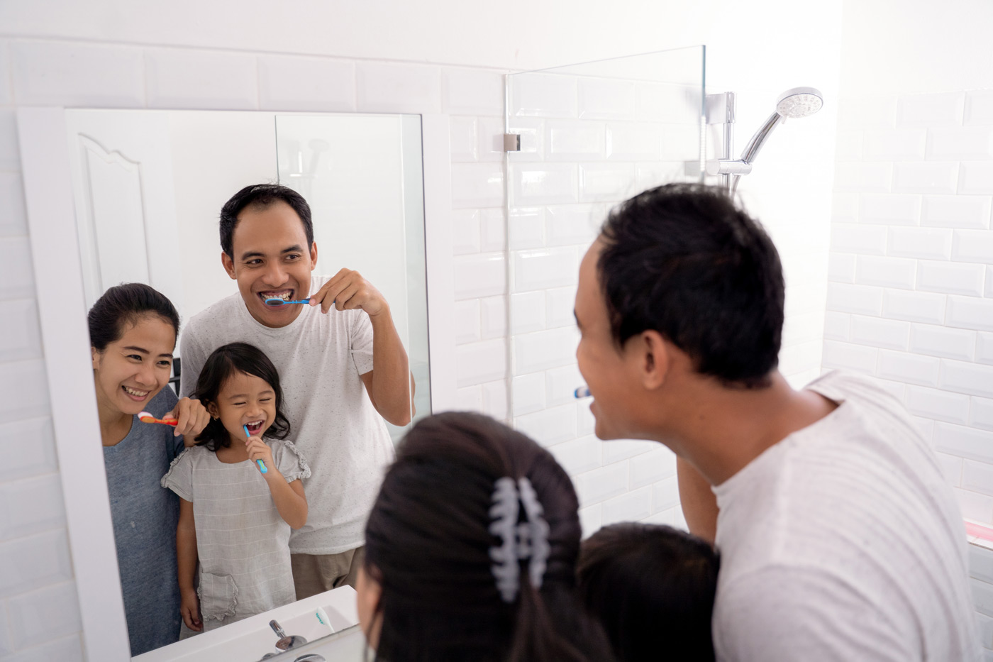 A family of three happily brushing their teeth together in a bathroom.
