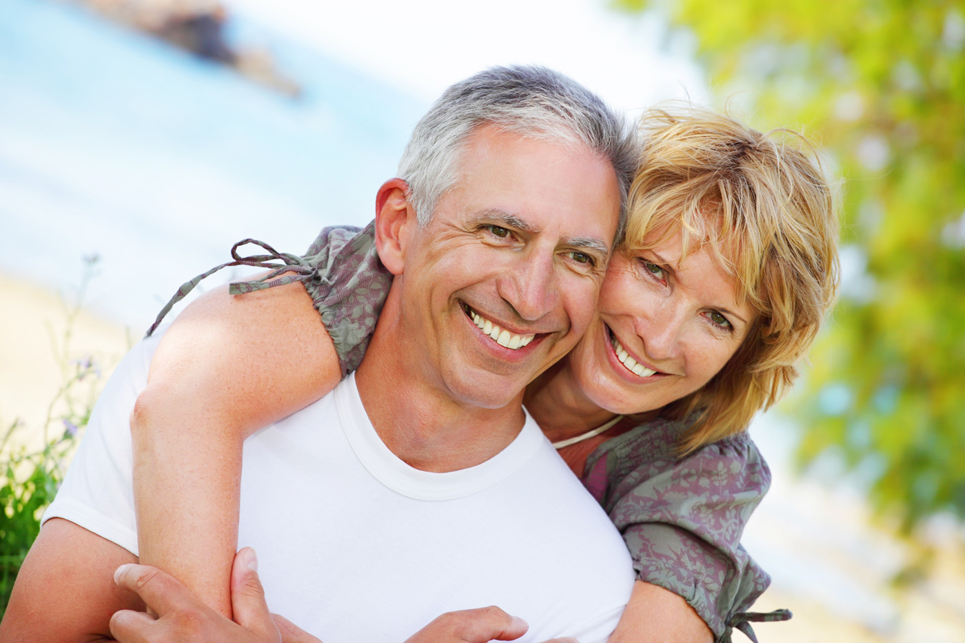 A smiling couple showing off their healthy teeth, radiating happiness in an outdoor setting.
