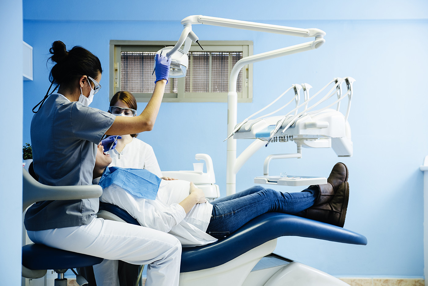 Dentist and assistant performing oral surgery on a patient in a dental chair with dental tools around.
