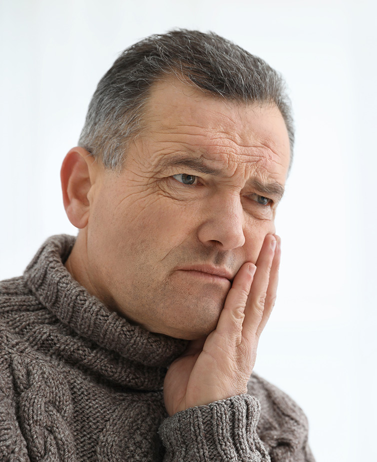 An man appearing to be in dental pain, holding their cheek and expressing discomfort.